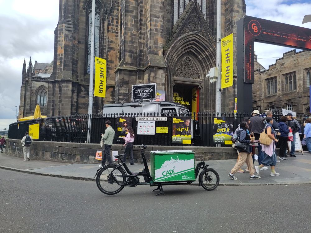 An urban cargo XL bike with Cadi Courier branding in front of the cathedral on the corner of Johnston Terrace and Castlehill.