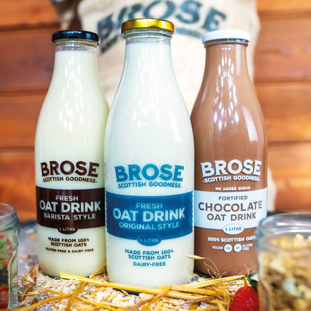 Three full Brose Oats glass bottles on a surface surrounded by flour, wheat stalks and a glass jar on either side protruding slightly into the frame.