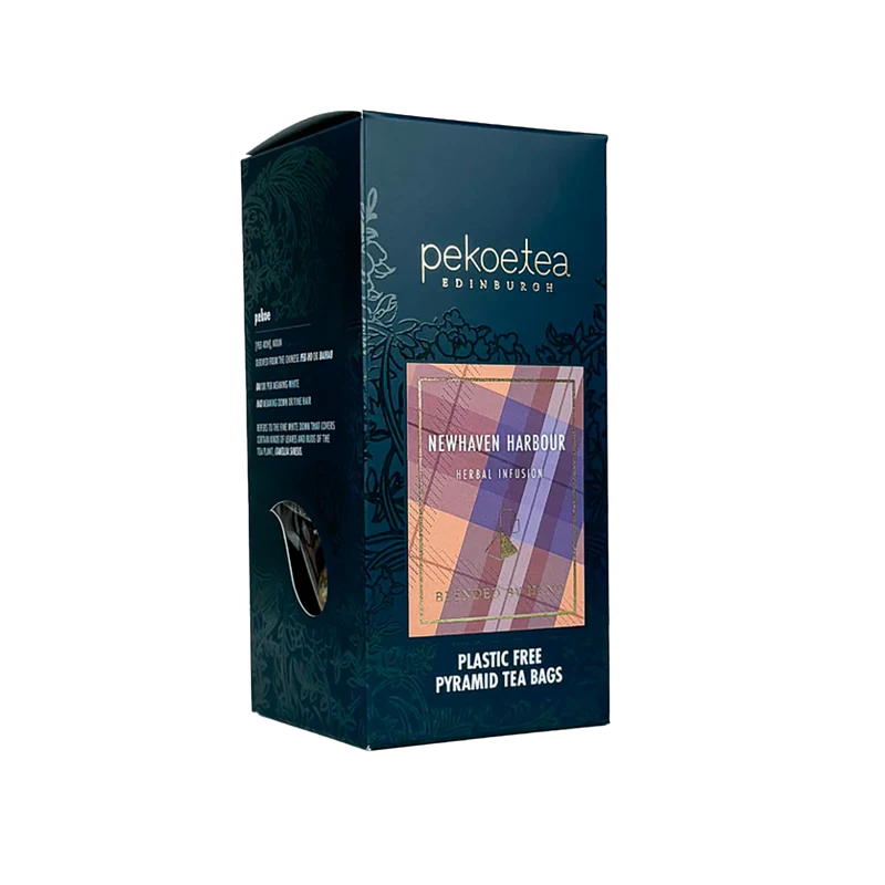 Cardboard box at an angle with two faces visible. On the front is the PekoeTea brand at the top and embossed decorations around the side, with an image of a tartan background below with Newhaven Harbour written over it in white text. At the bottom is written plastic free pyramid tea bags.